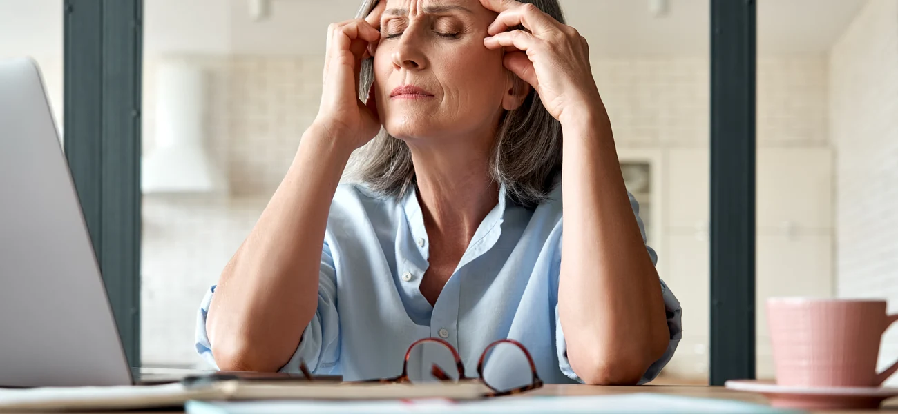 Woman in her fifties at a laptop at home, rubbing her temples during menopause symptoms